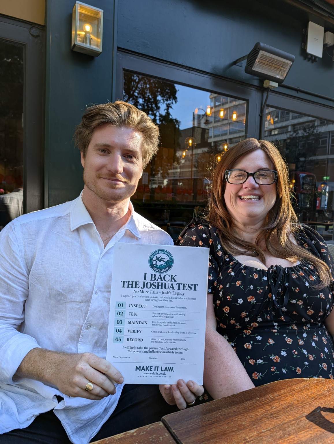 Two people smiling and holding The Joshua Test campaign pledge during a meeting in Holborn